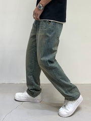Men's loose-fit jeans in blue-green wash cotton, styled casually.