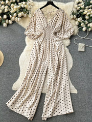 Beige polka dot smocked wide-leg romper with V-neck and tie detail.
