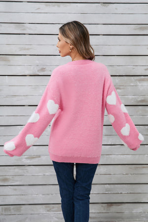 Pink fluffy knit sweater with white heart detail on sleeves.