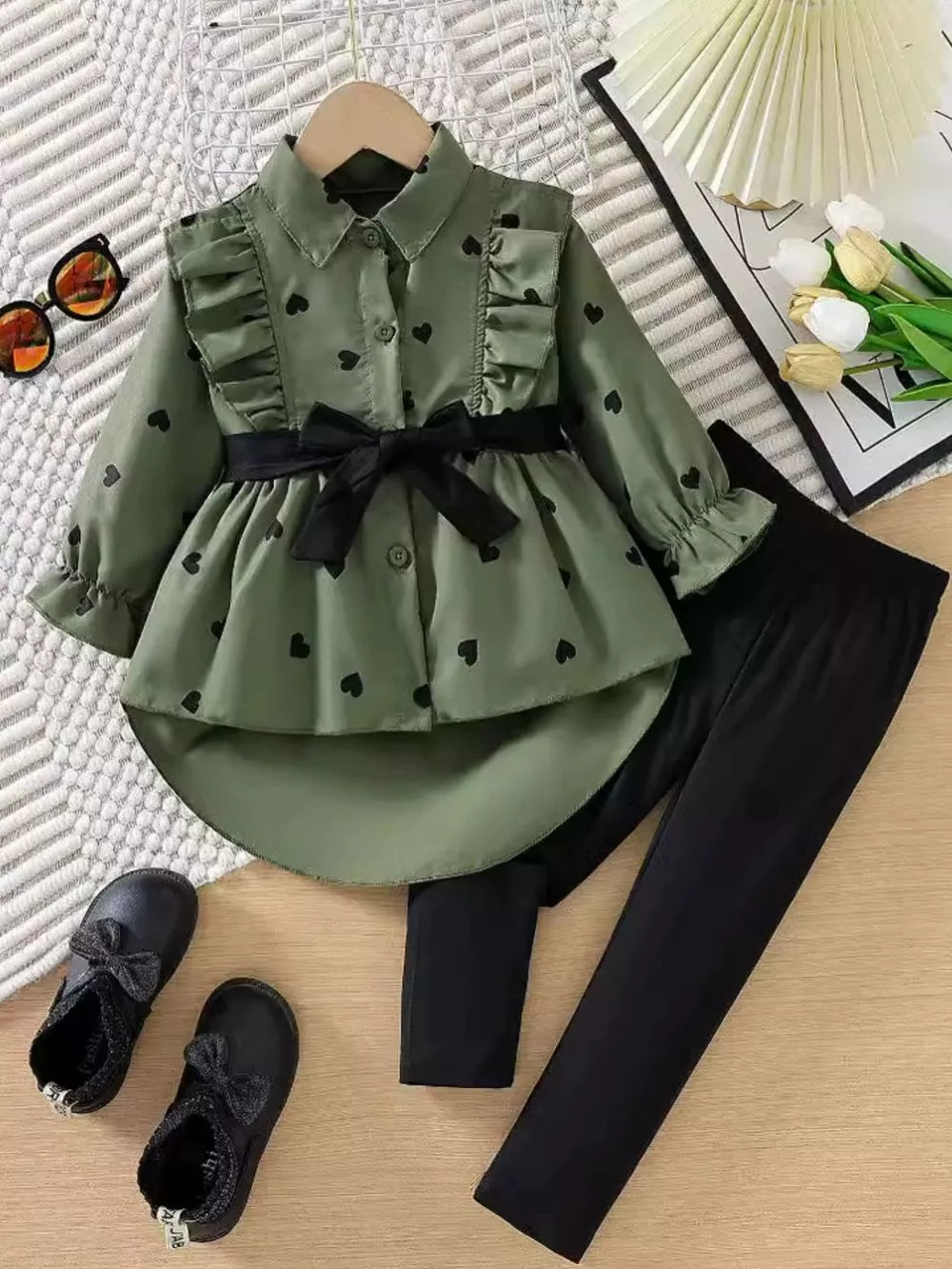 Toddler girls' green heart print ruffle shirt with black bow belt and black leggings.