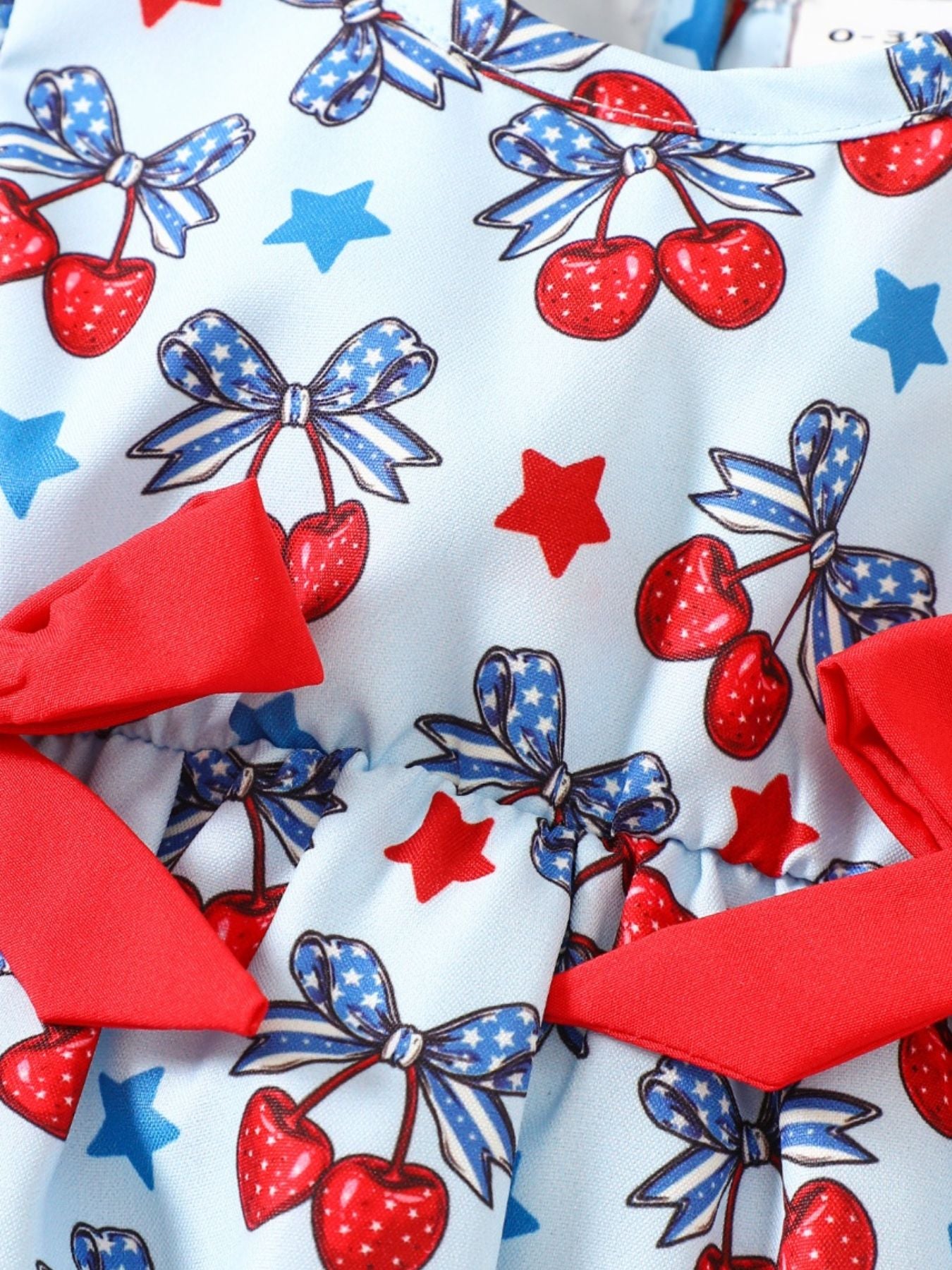 Baby one-piece with cherry, bow, and star print in light blue cotton, featuring red ruffle trim.