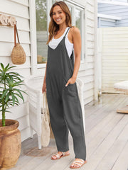 Relaxed dark gray pocketed overalls jumpsuit with a white tank top and sandals.