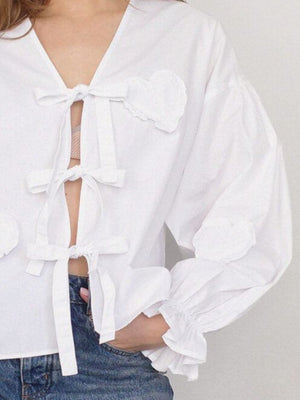 White blouse with heart appliqué and tie front, ruffled cuffs.