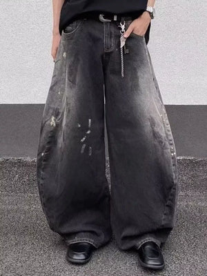 Men's black wide leg distressed jeans with paint splatters and a chain detail.