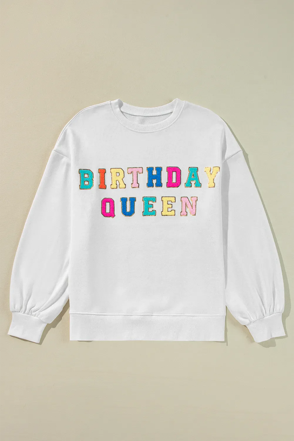 White sweatshirt with puff sleeves and colorful "Birthday Queen" text graphic.