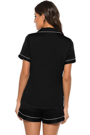 Black satin pajama set with white piping, short sleeves, and shorts.