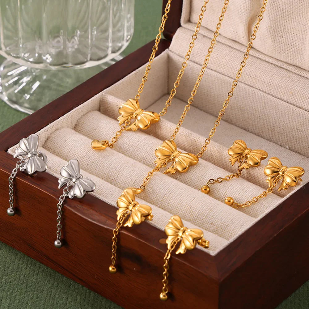 Gold bow and heart drop necklaces with delicate chains, displayed in a jewelry box.