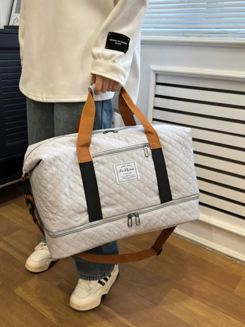 Creamy-white quilted travel duffel bag with brown straps and black accents.