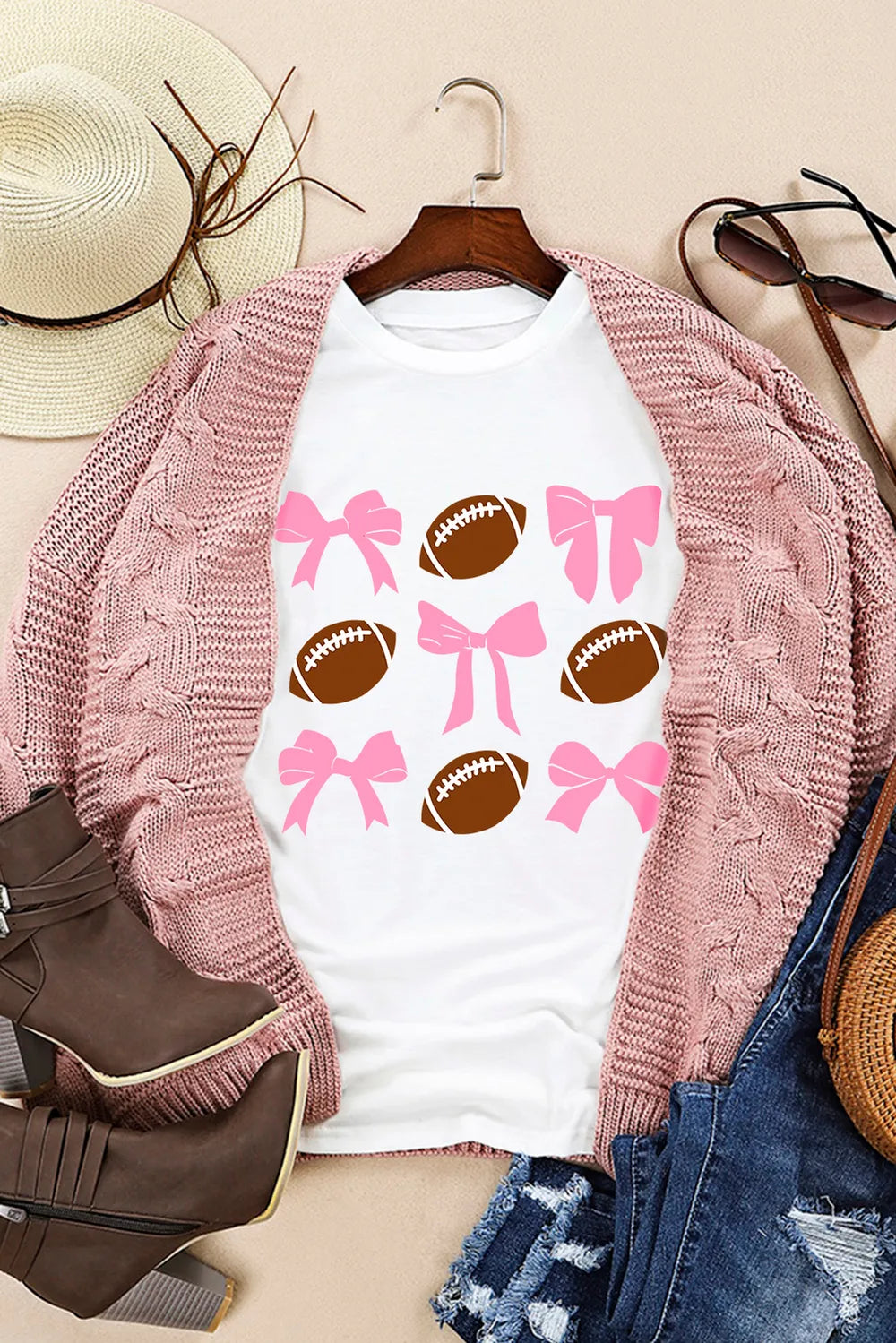 White graphic tee with a pattern of pink bows and brown footballs.