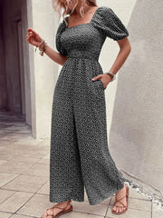 Black floral smocked bodice wide-leg jumpsuit with puff sleeves and square neckline.