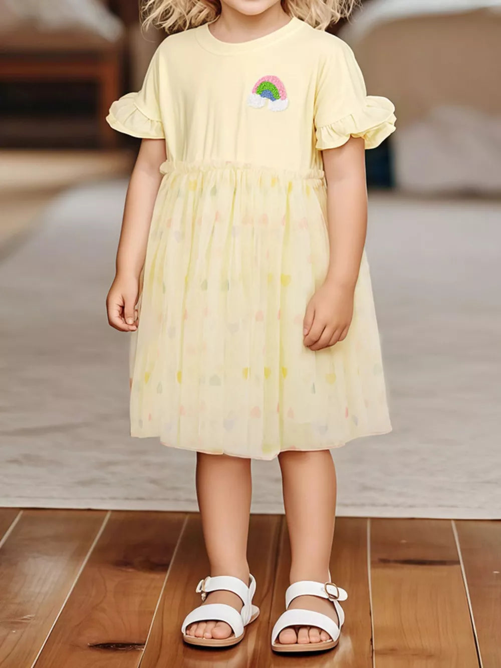 Yellow baby dress with rainbow applique, ruffled sleeves, and tulle skirt with heart pattern.