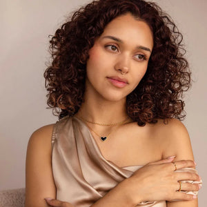 Gold chain necklace with a black heart pendant and beaded detail