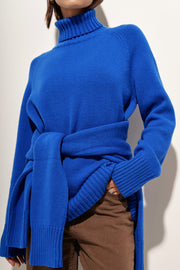 Royal blue cashmere turtleneck sweater with raglan sleeves and a tie waist detail.