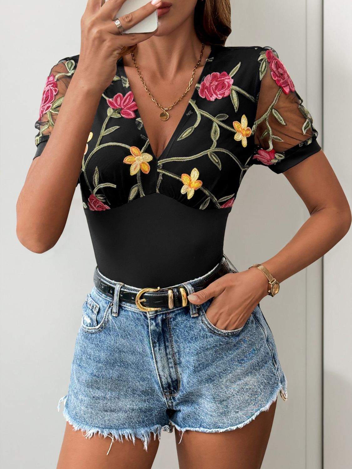 Black bodysuit with embroidered floral mesh sleeves and V-neck.