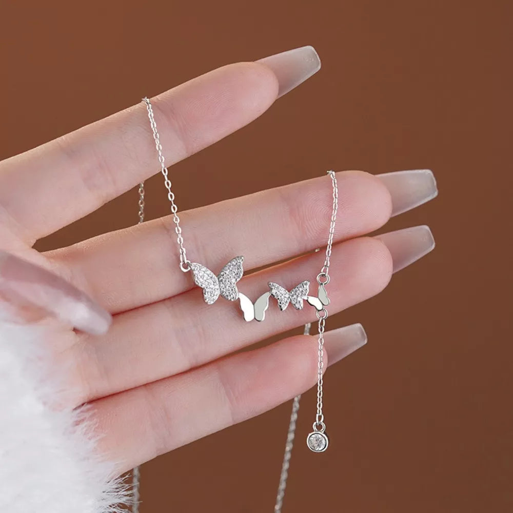 Delicate silver necklace with sparkling zircon butterfly charms and a dangling crystal accent.