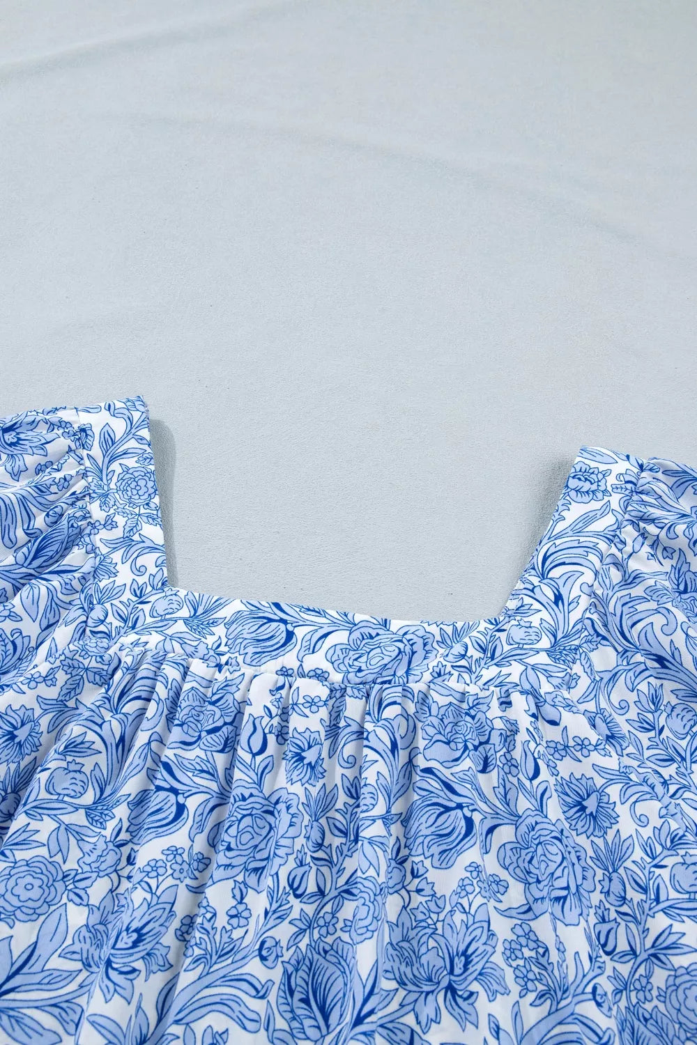 Floral pleated blouse with square neckline in blue and white floral print polyester.