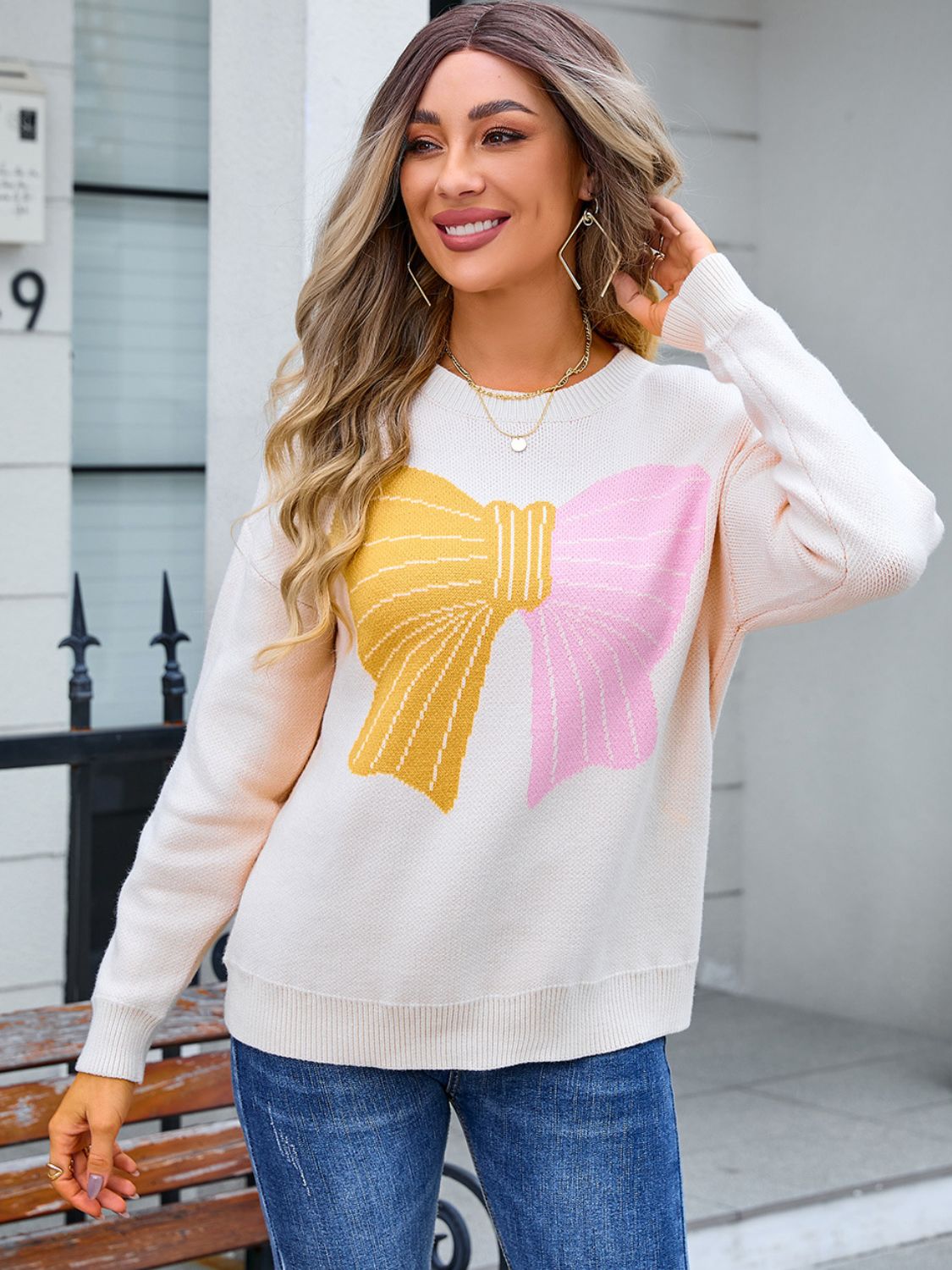 Ivory knit sweater with a large yellow and pink bow graphic, crew neck, long sleeves.