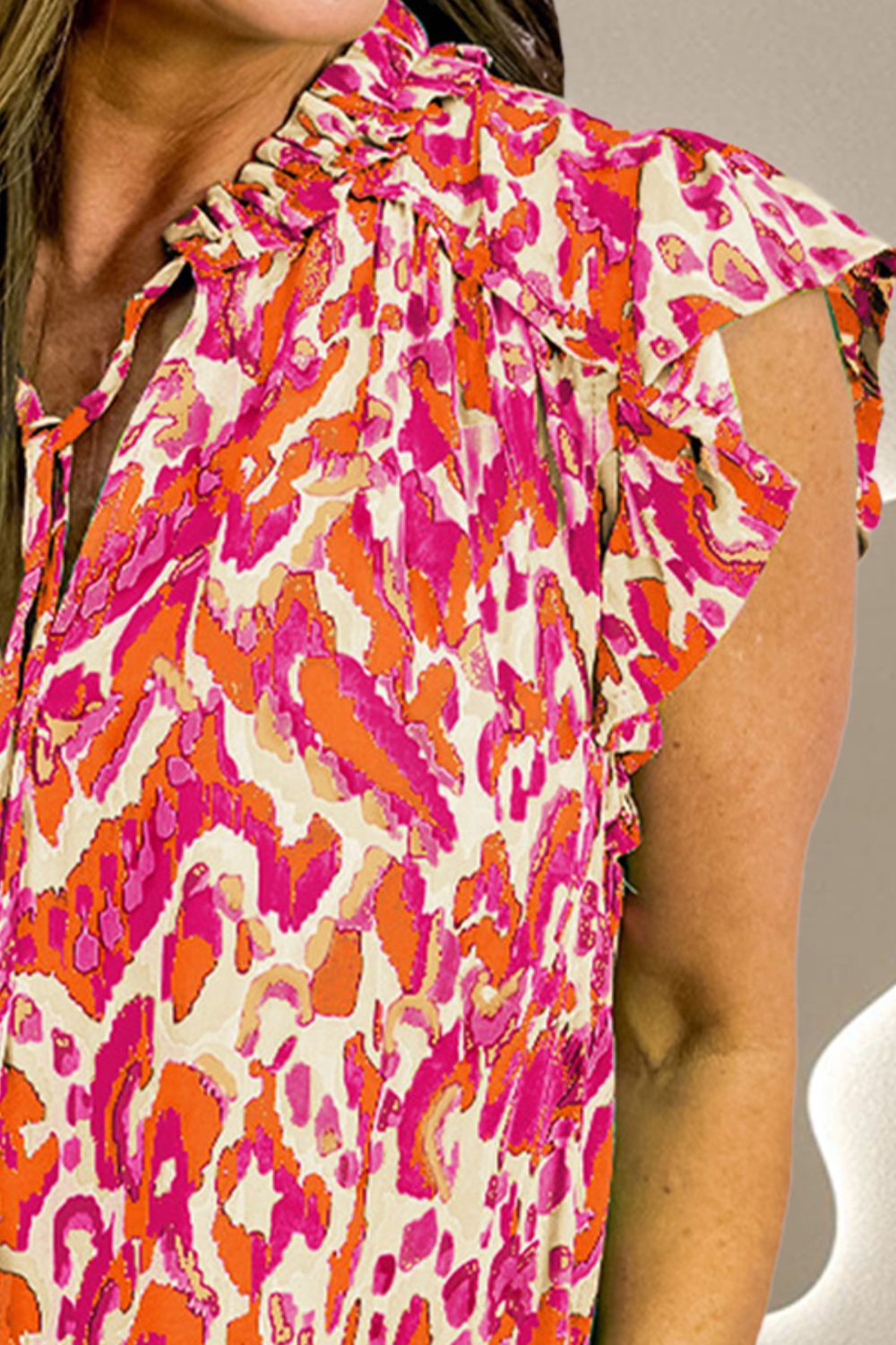 Printed ruffle cap-sleeve blouse in abstract print, featuring a tie-neck and ruffled cap sleeves.