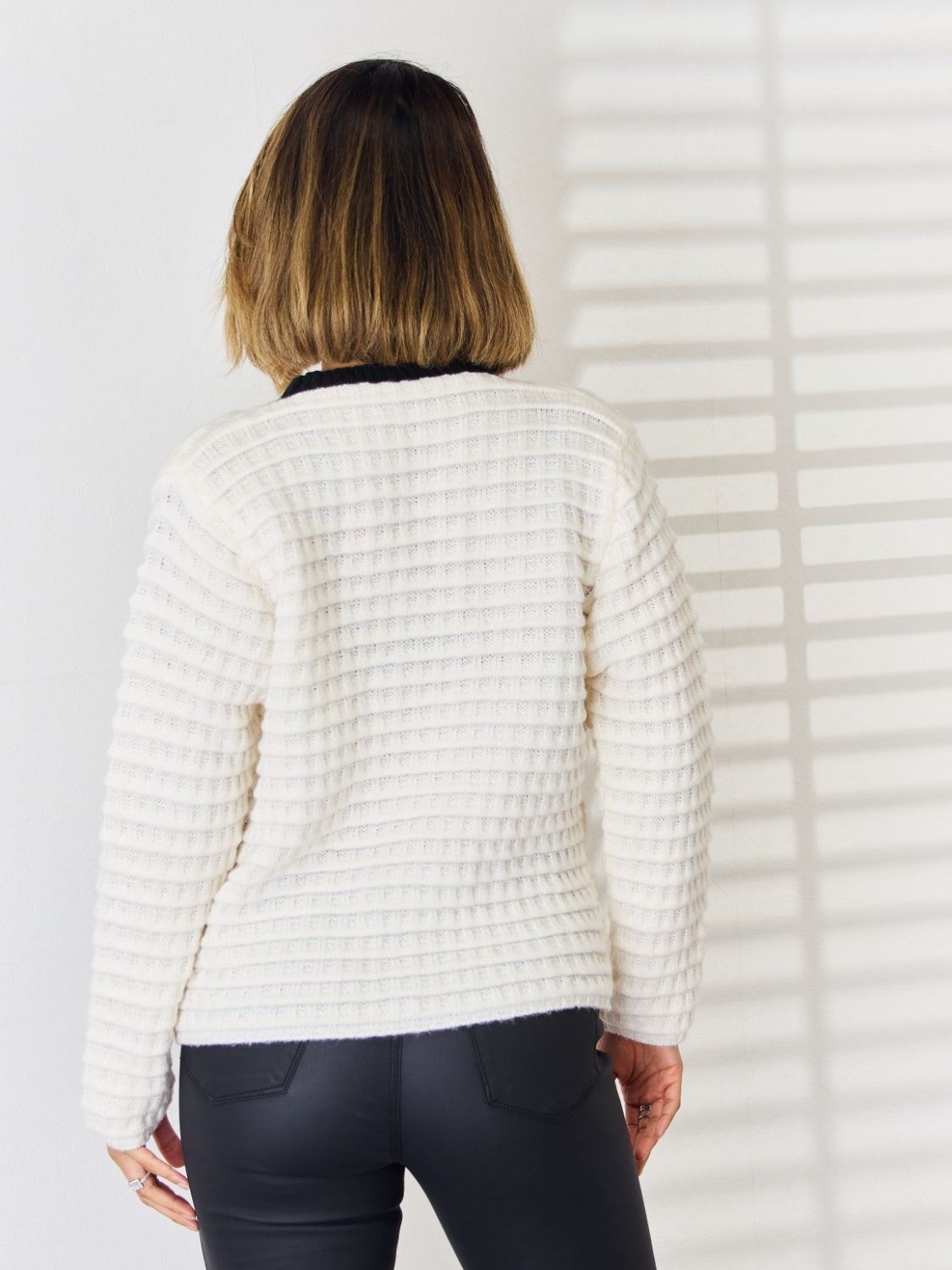 Textured knit white cardigan with contrast black trim and button front detail.