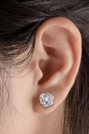 Silver rose stud earrings with a diamond center, worn by a woman.