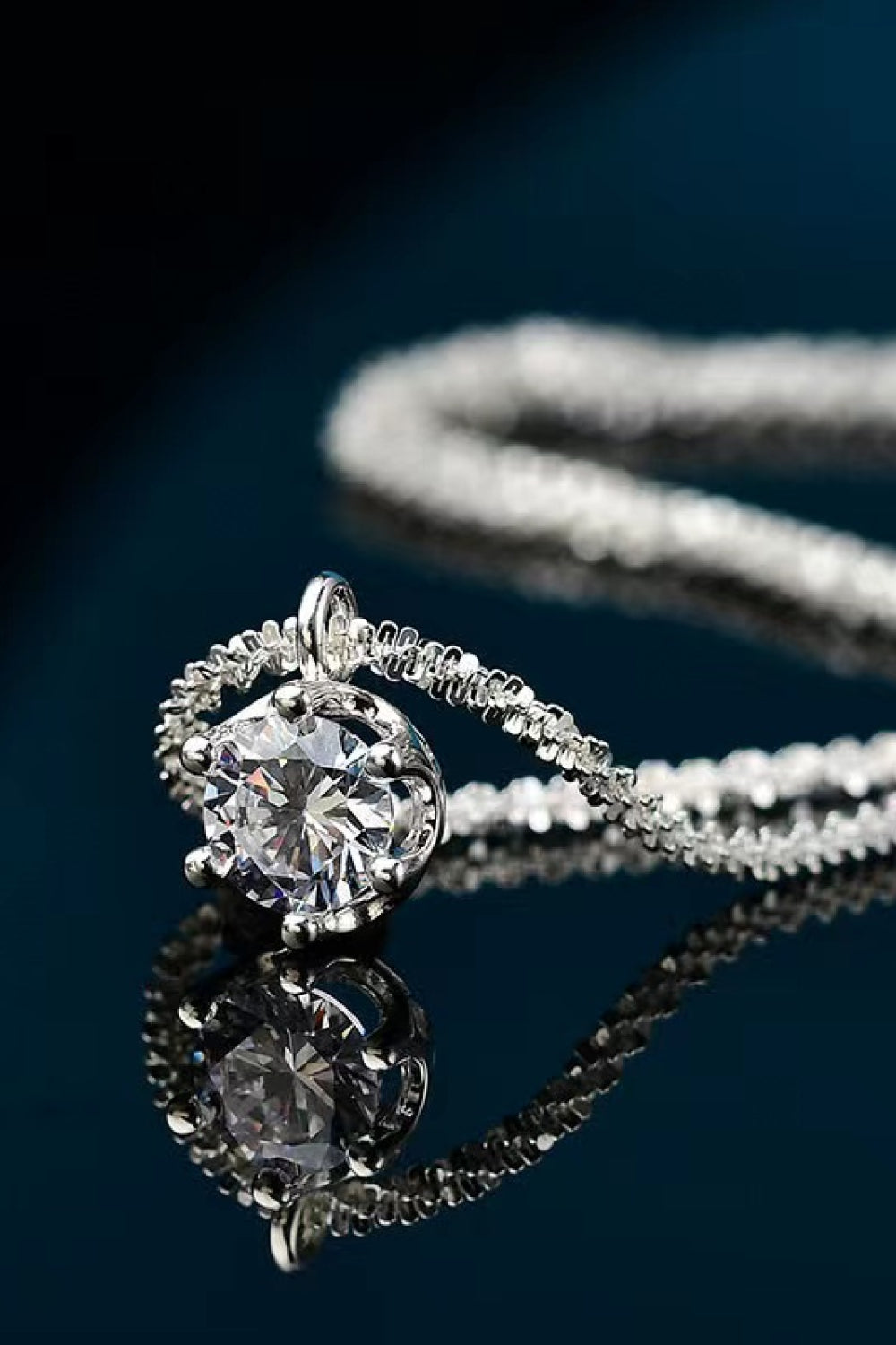Silver pendant necklace with a round moissanite stone in a textured halo setting.