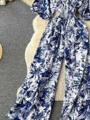 Tropical print smocked wide-leg romper in dark blue and white, featuring puff sleeves and a flowy silhouette.