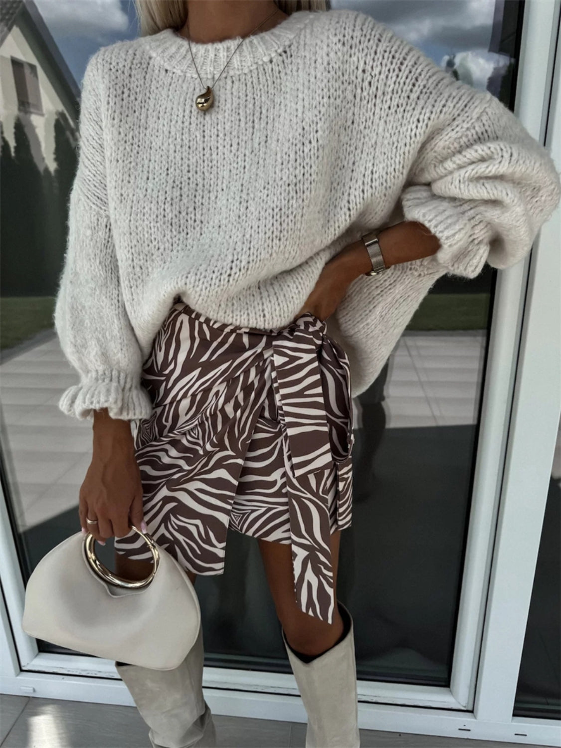 Cream voluminous sleeve knit sweater with ruffled cuffs, paired with a zebra print wrap skirt.