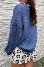 Dusty blue knit crewneck sweater with white contrast stitching at neckline and hem.
