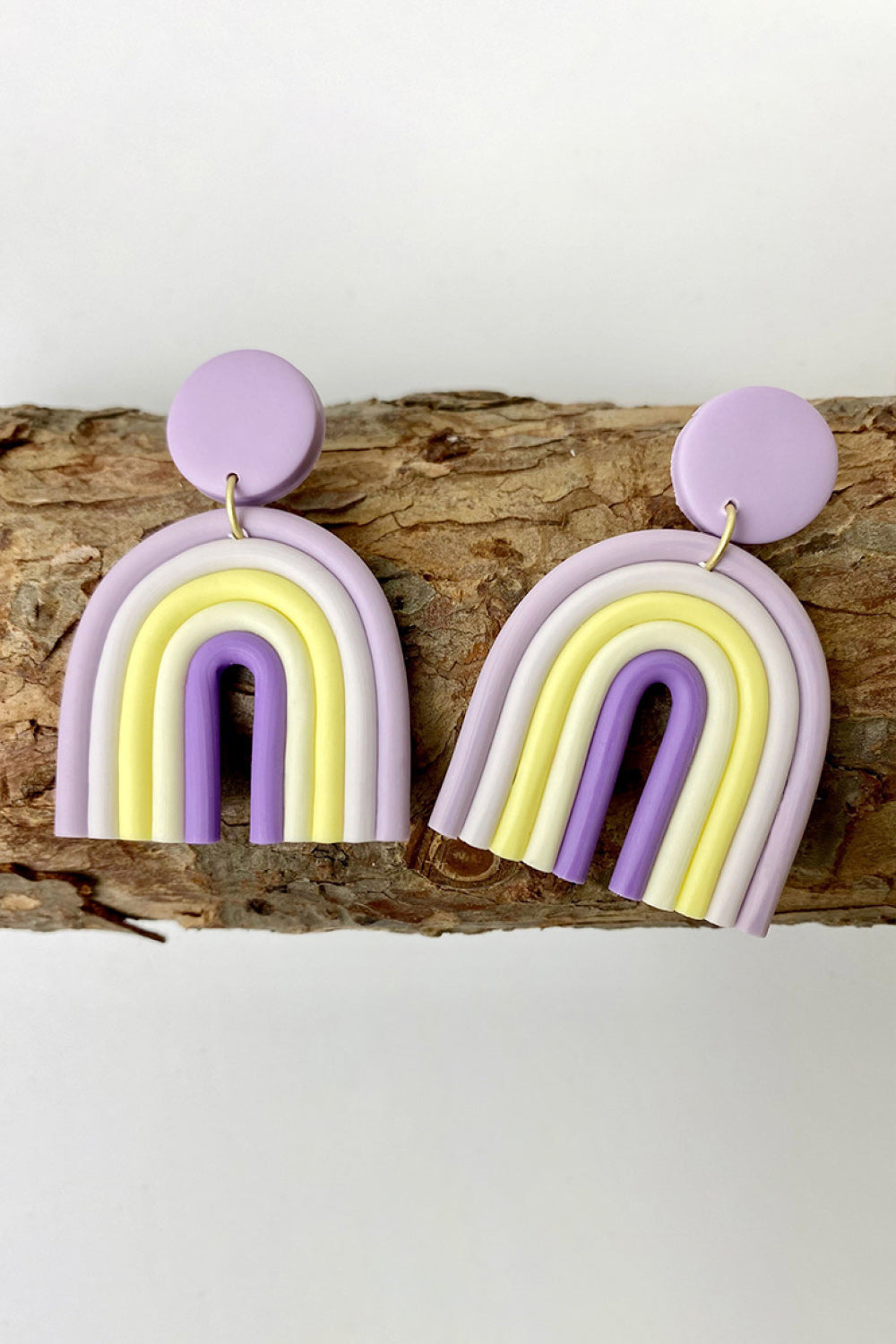 Rainbow arch clay earrings in lavender, yellow, and white with purple accents.