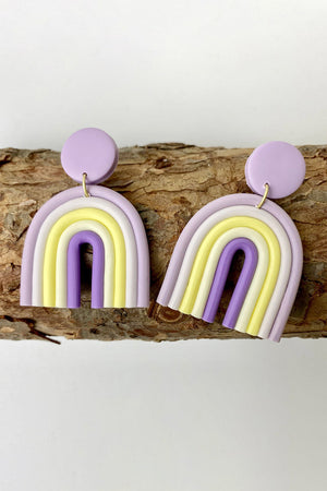 Rainbow arch clay earrings in lavender, yellow, and white with purple accents.