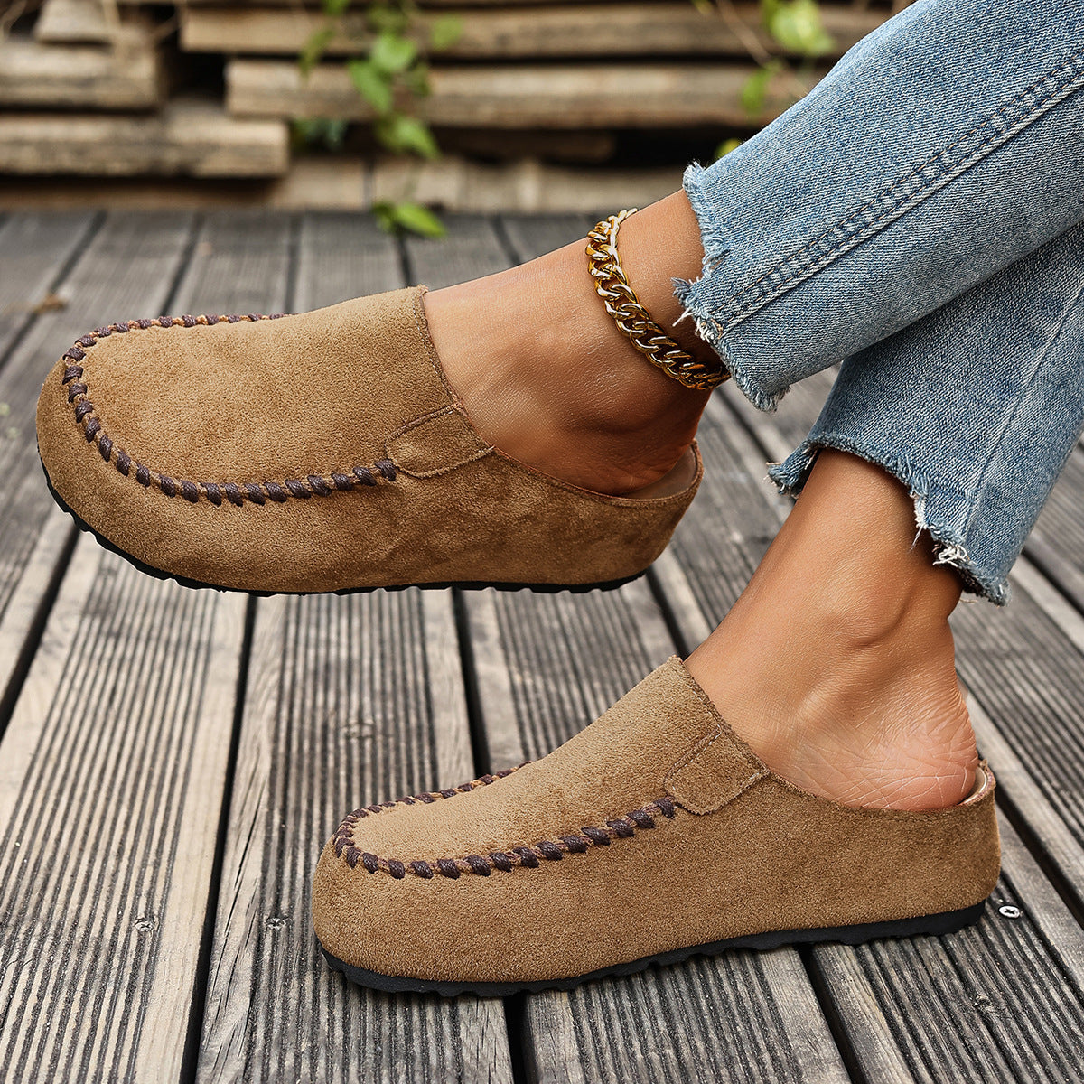 Brown slip-on flats with round toe and decorative stitching, styled with jeans and an anklet.