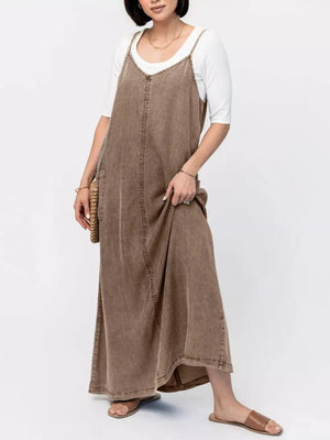 Brown washed denim maxi dress with V-neck and adjustable straps, styled with a white tee.