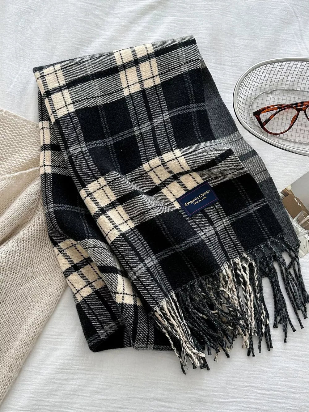 Black plaid scarf with fringe and cream accents, featuring a classic tartan pattern.