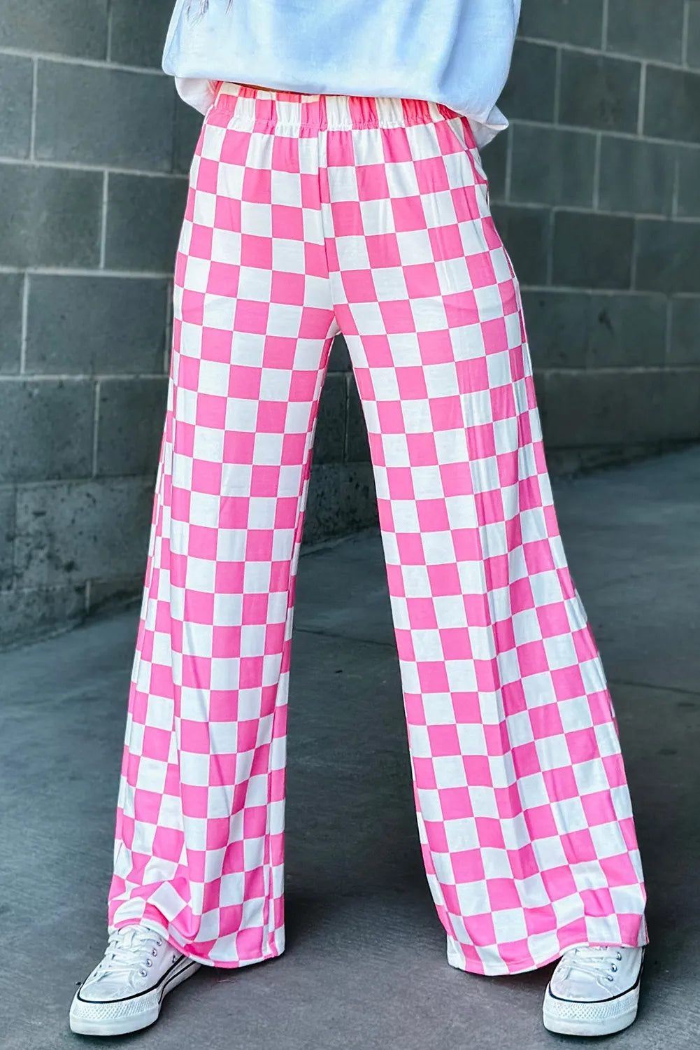 Checkerboard palazzo trousers in fuchsia pink and white, with a wide leg and elastic waist.