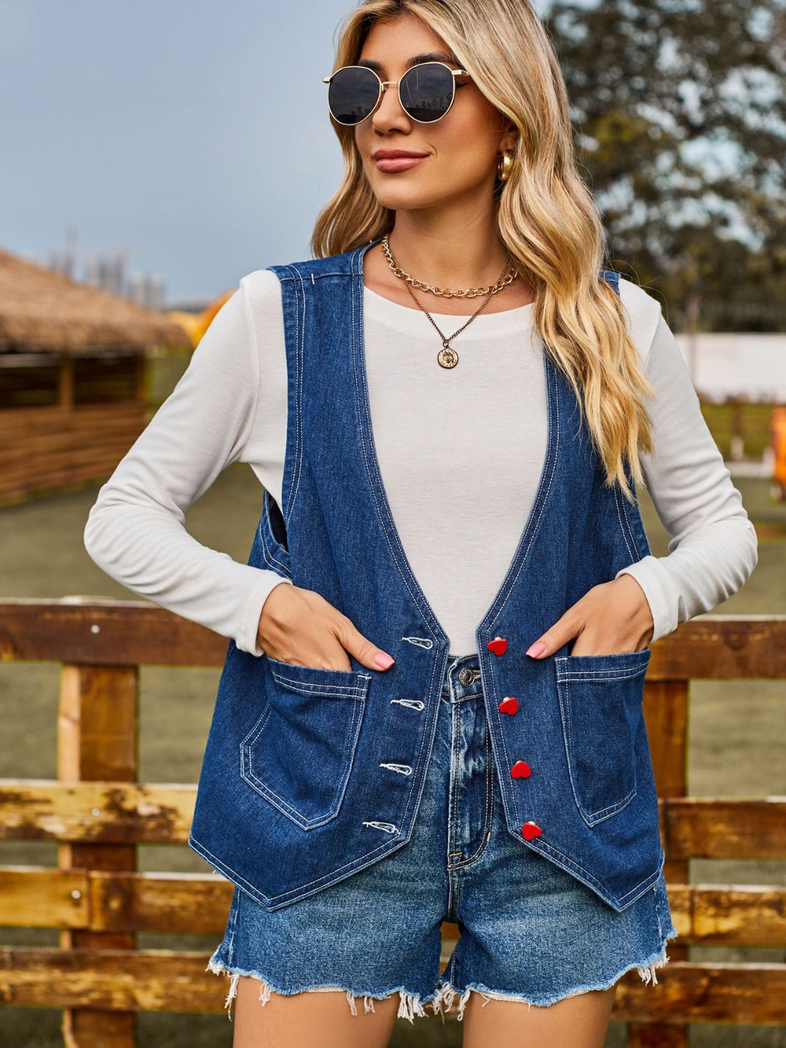 Indigo denim vest with red heart buttons and chest pockets, worn over a white long-sleeve shirt.