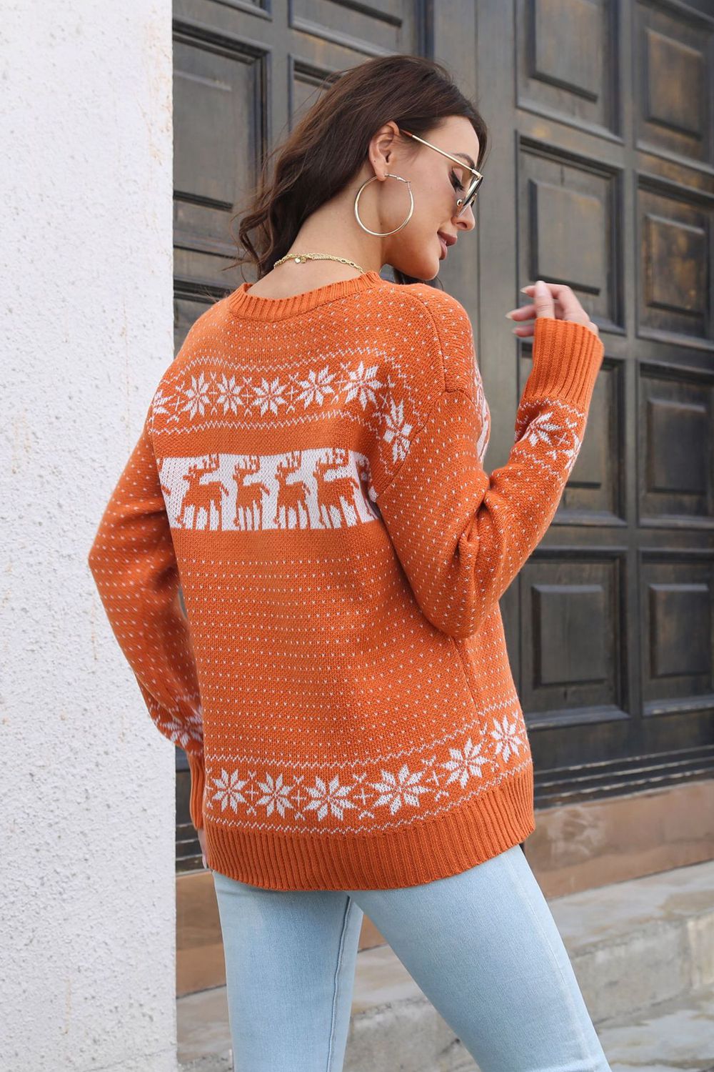 Orange reindeer jacquard knit sweater with snowflake pattern and crew neck.