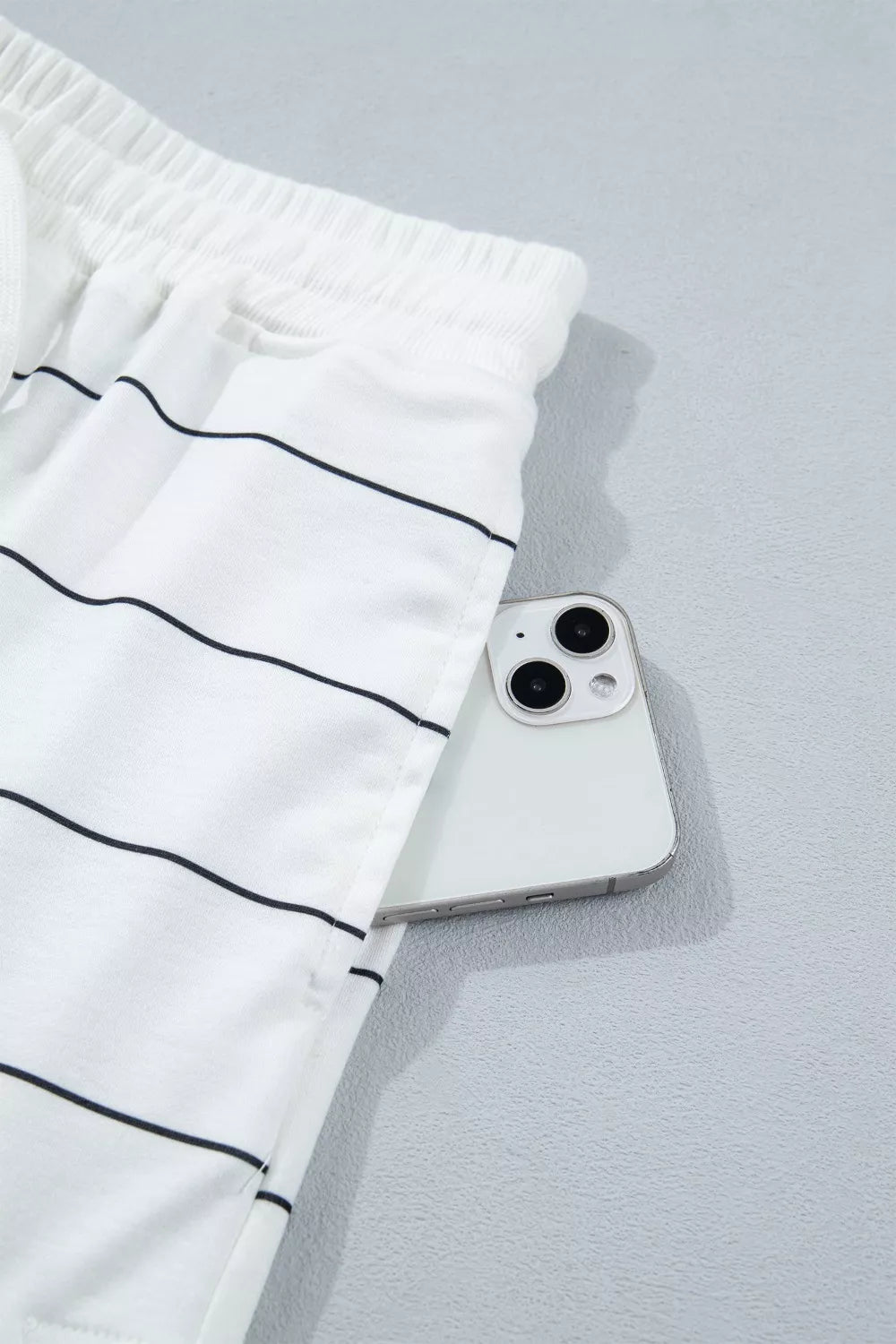 White polyester shorts with black stripes and drawstring waist, showing a pocket detail.