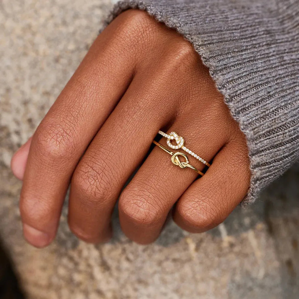 Gold knot rings, one with pavé detail, 18K gold-plated, stacked on a finger.