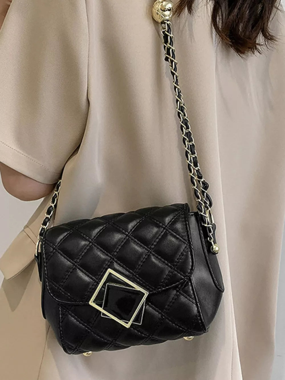 Black quilted crossbody bag with gold chain strap and square buckle detail.