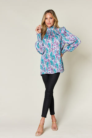 High neck abstract print blouse in red-violet and sky blue with smocked cuffs and shoulders.