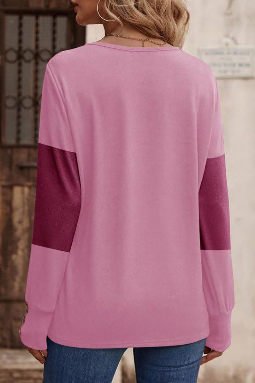 Pink knit sweater with contrasting red-violet sleeves and button cuffs.
