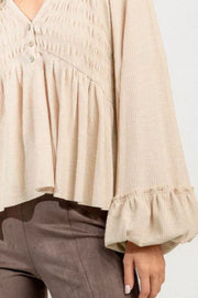 Tan textured ribbed peplum blouse with smocked bodice and ruffled cuffs.