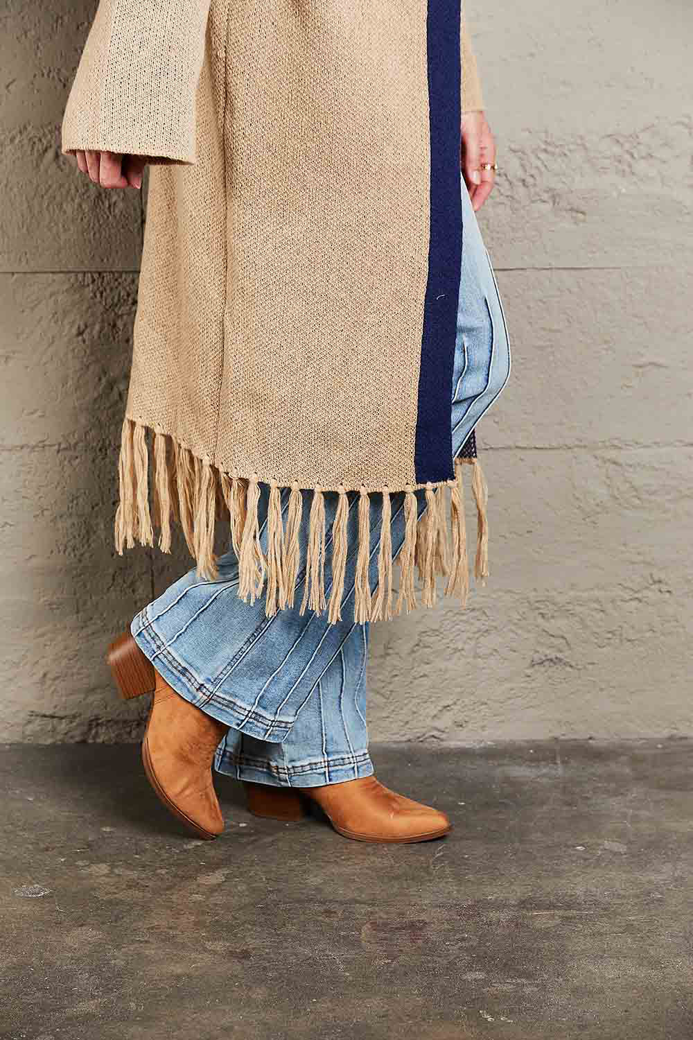 Khaki cardigan with fringe hem and navy trim, styled with flared jeans and boots.