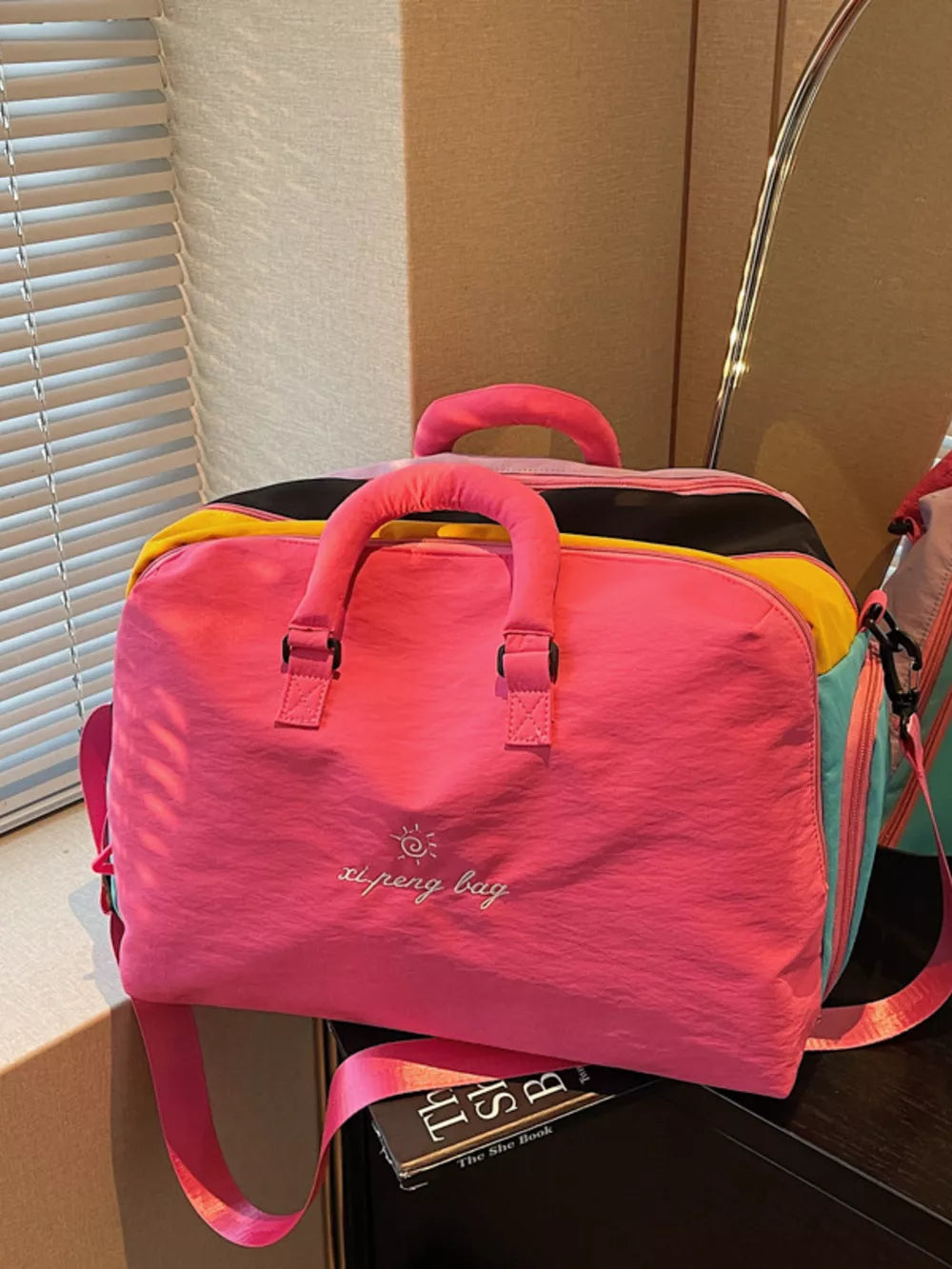 Vibrant pink duffel bag with embroidered text and multicolor accents, featuring top handles and a crossbody strap.