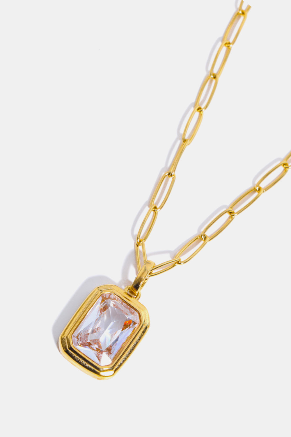 Gold paperclip chain necklace with a rectangular transparent crystal pendant.