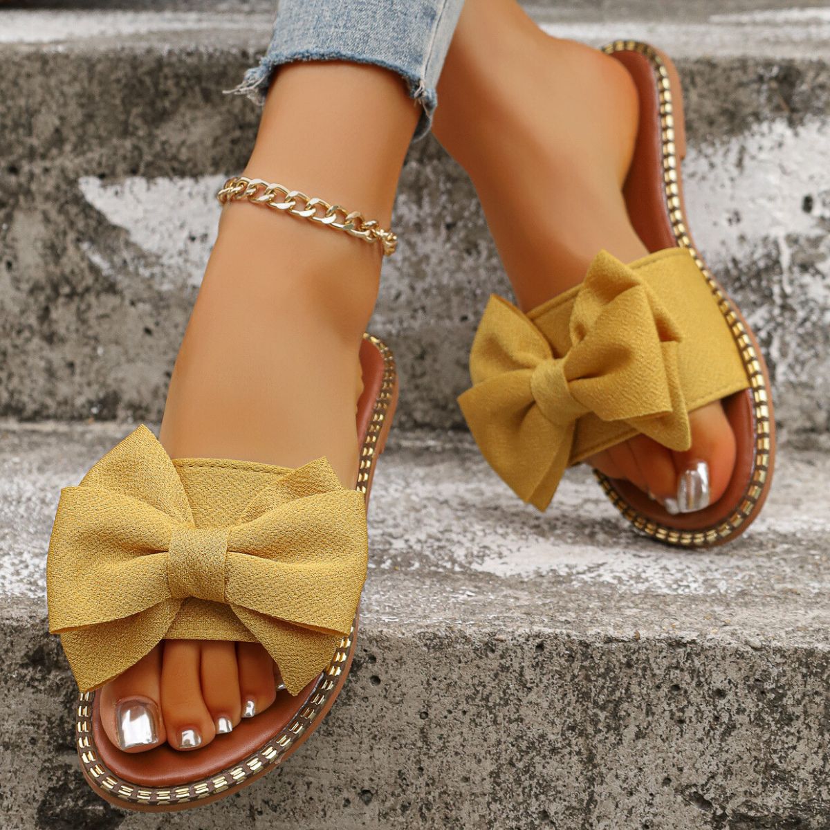 Yellow bowknot slide sandals with gold trim and a gold anklet.