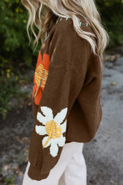 Brown knit sweater with embroidered floral detail on sleeve and shoulder.