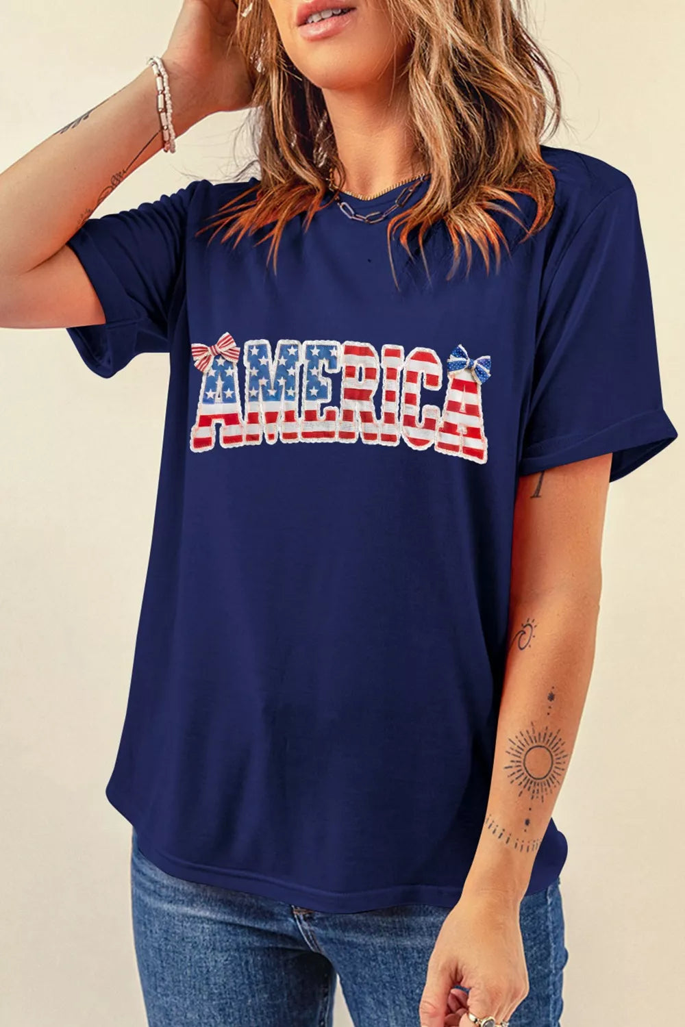 Navy patriotic graphic t-shirt with "AMERICA" text and bow details, short sleeves, relaxed fit.