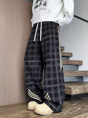 Men's black wide leg plaid sweatpants with white drawstring and side stripe detail.