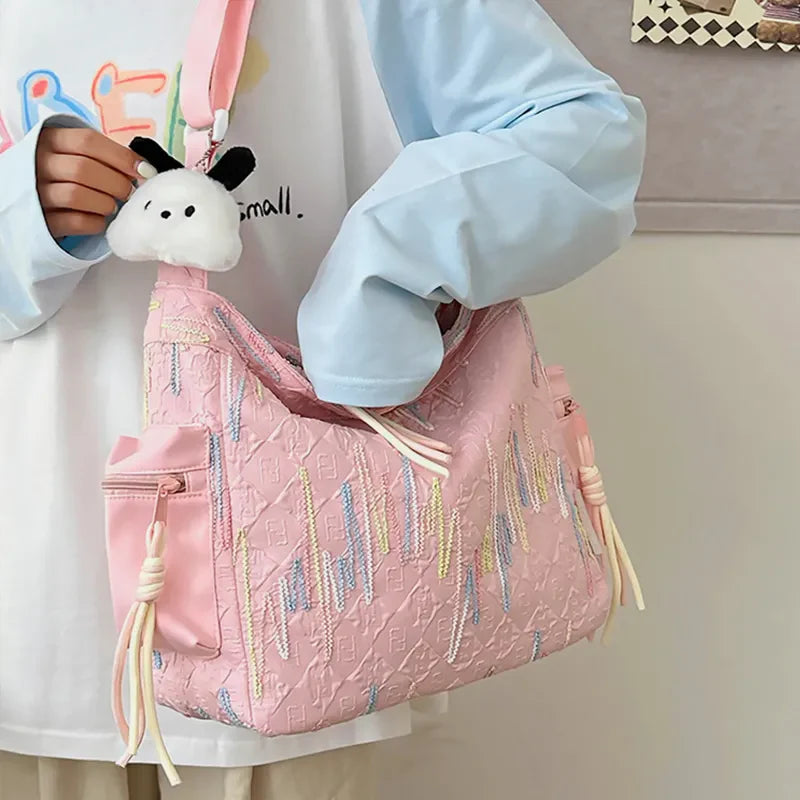 Pink slouchy shoulder bag with embroidered pattern and tassel details, featuring a cute plush charm.